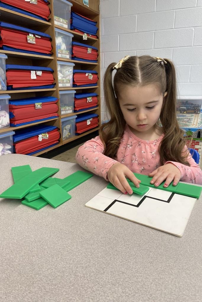 Girl solving green tangram puzzle in classroom